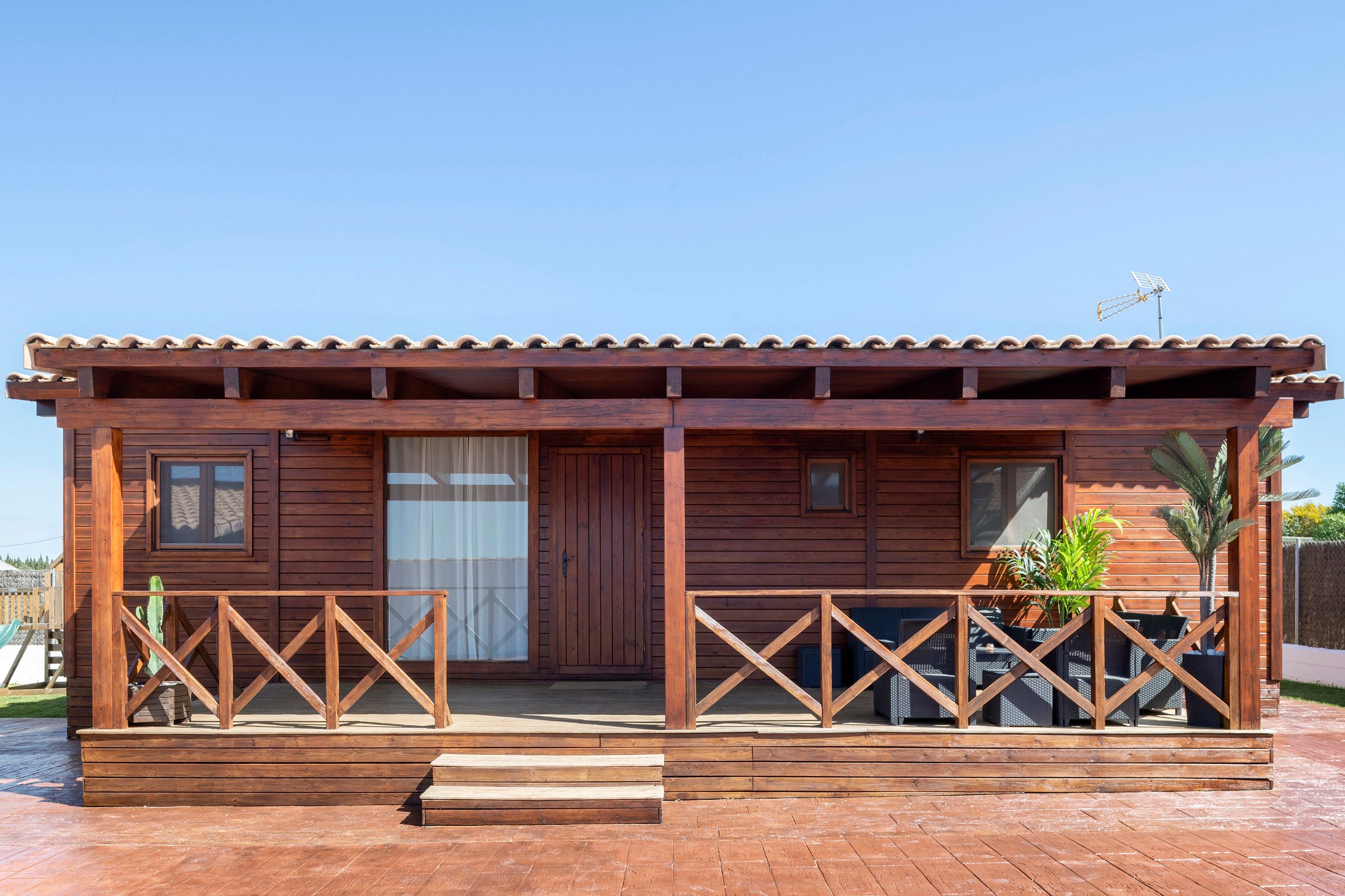 Une cabane en bois avec un toit recouvert de tuiles, une porte d’entrée et un petit porche doté d’une balustrade.
