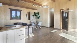 A wooden interior with a ceiling fan, a dining area with chairs, a kitchen visible through an open door, and a large mirror on the wall.