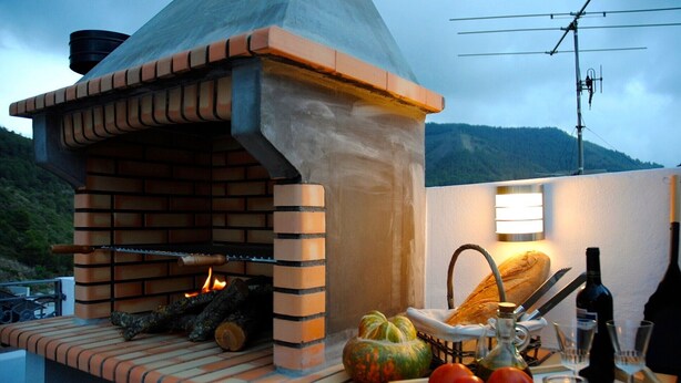 Ein Backofen aus Ziegelsteinen mit Schornstein, ein Tisch mit Brot, Tomaten, einer Flasche und einer Kerze.
