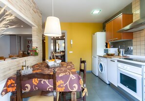Ett modernt kök med en matplats, inklusive ett bord med ett blommigt bordsduk, en tvättmaskin och ett kylskåp.