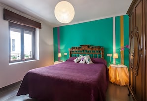 Une chambre avec un lit, une fenêtre, une tête de lit en bois, une table de chevet et une armoire.