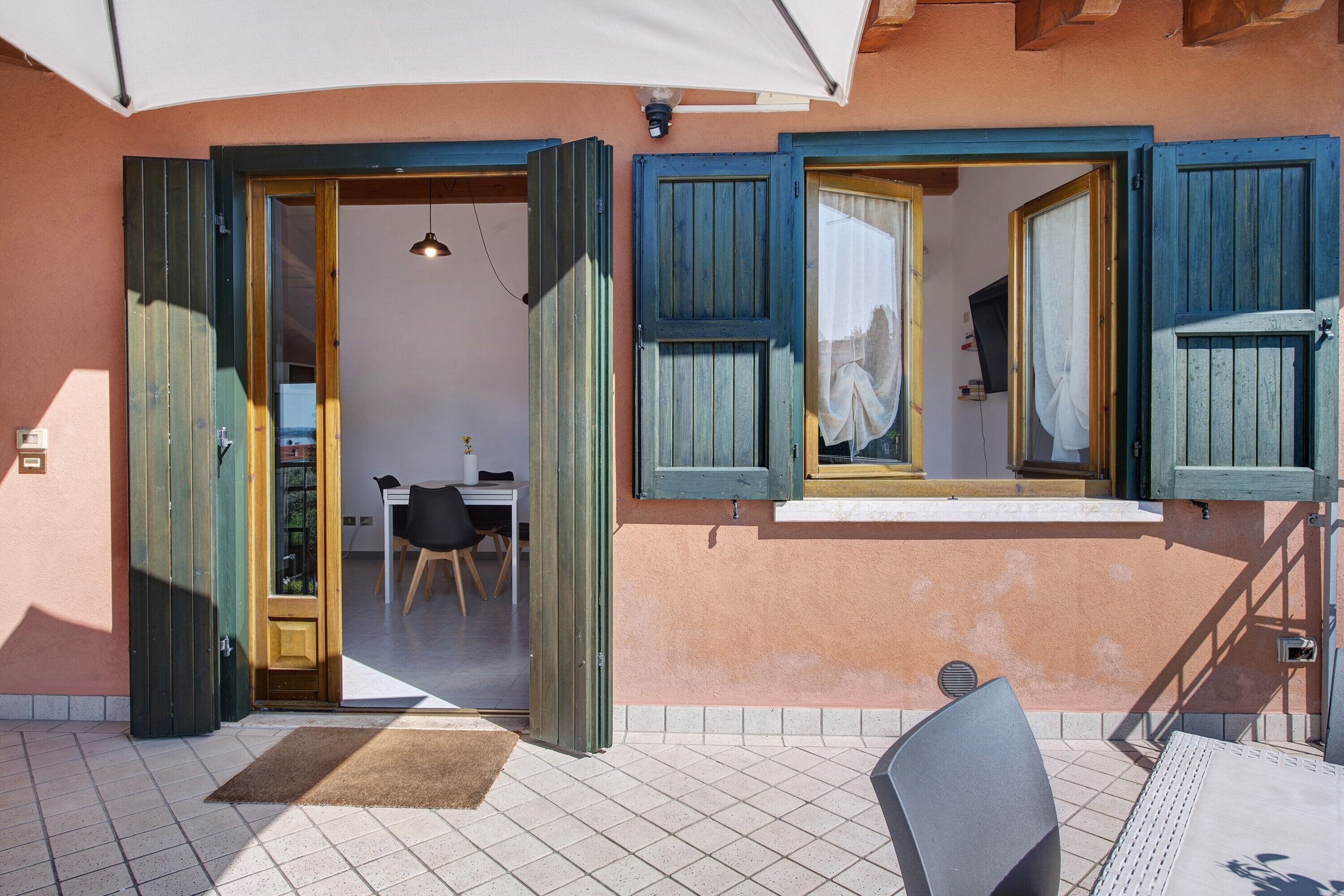 A room with a tiled floor, a chair, a table, and a window with wooden shutters.
