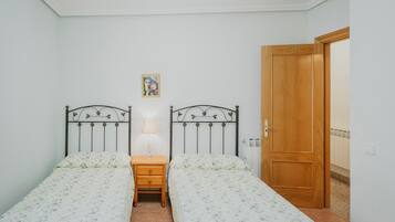 A room with two single beds, a bedside table with a lamp, a wooden door, and a small framed picture on the wall.