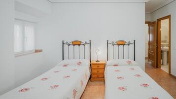 Une chambre avec deux lits simples, une table de chevet, une fenêtre avec des rideaux et une porte donnant sur une salle de bain.