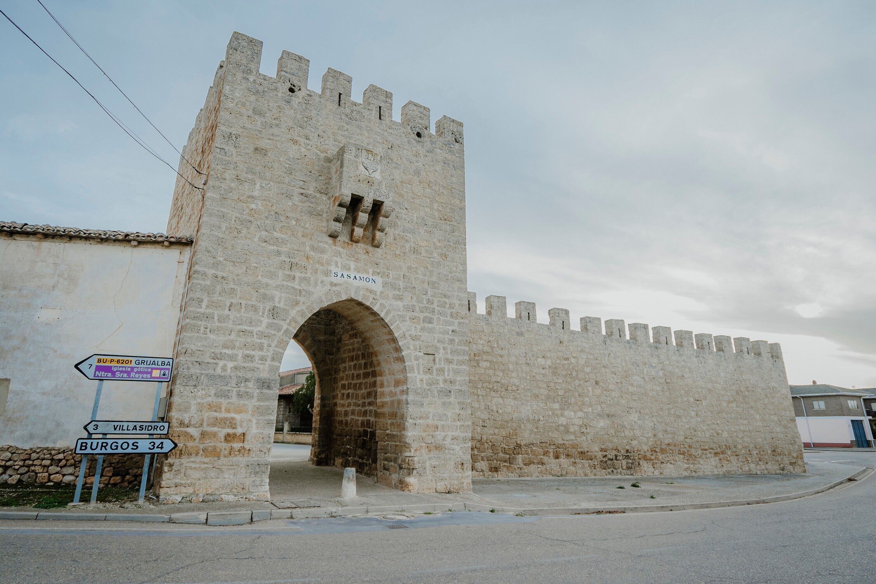 A stone castle entrance with a sign indicating directions to nearby locations.