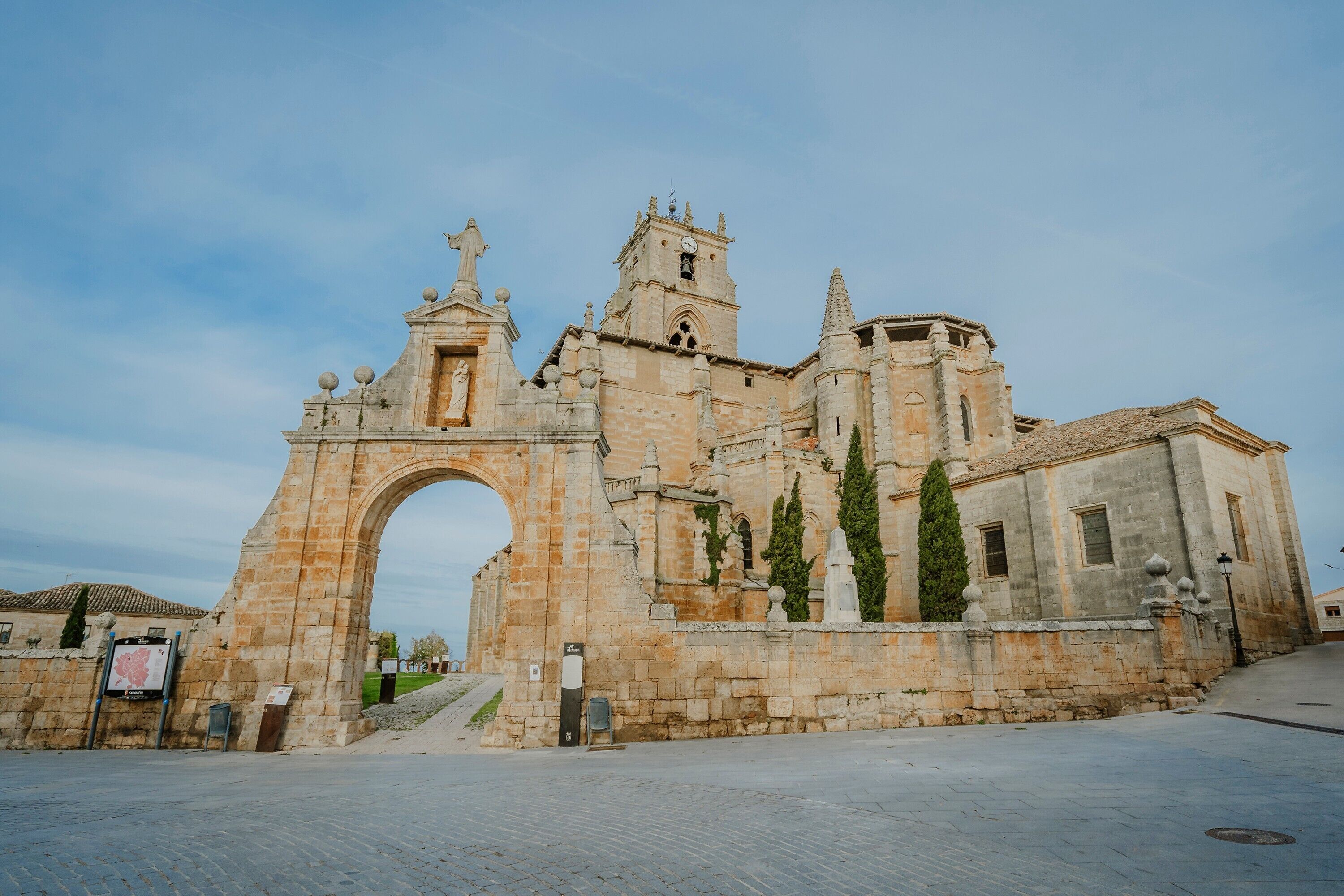 A historic stone building with an archway entrance, a bell tower, and a statue.