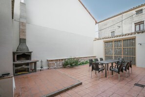 A patio with a stone fireplace, a table with chairs, and a window with wooden shutters. - Country House 'El Humilladero' with Private Terrace (Sasamón)