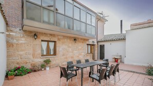 Un edificio in pietra con un'ampia finestra, un patio piastrellato e un tavolo con sedie.