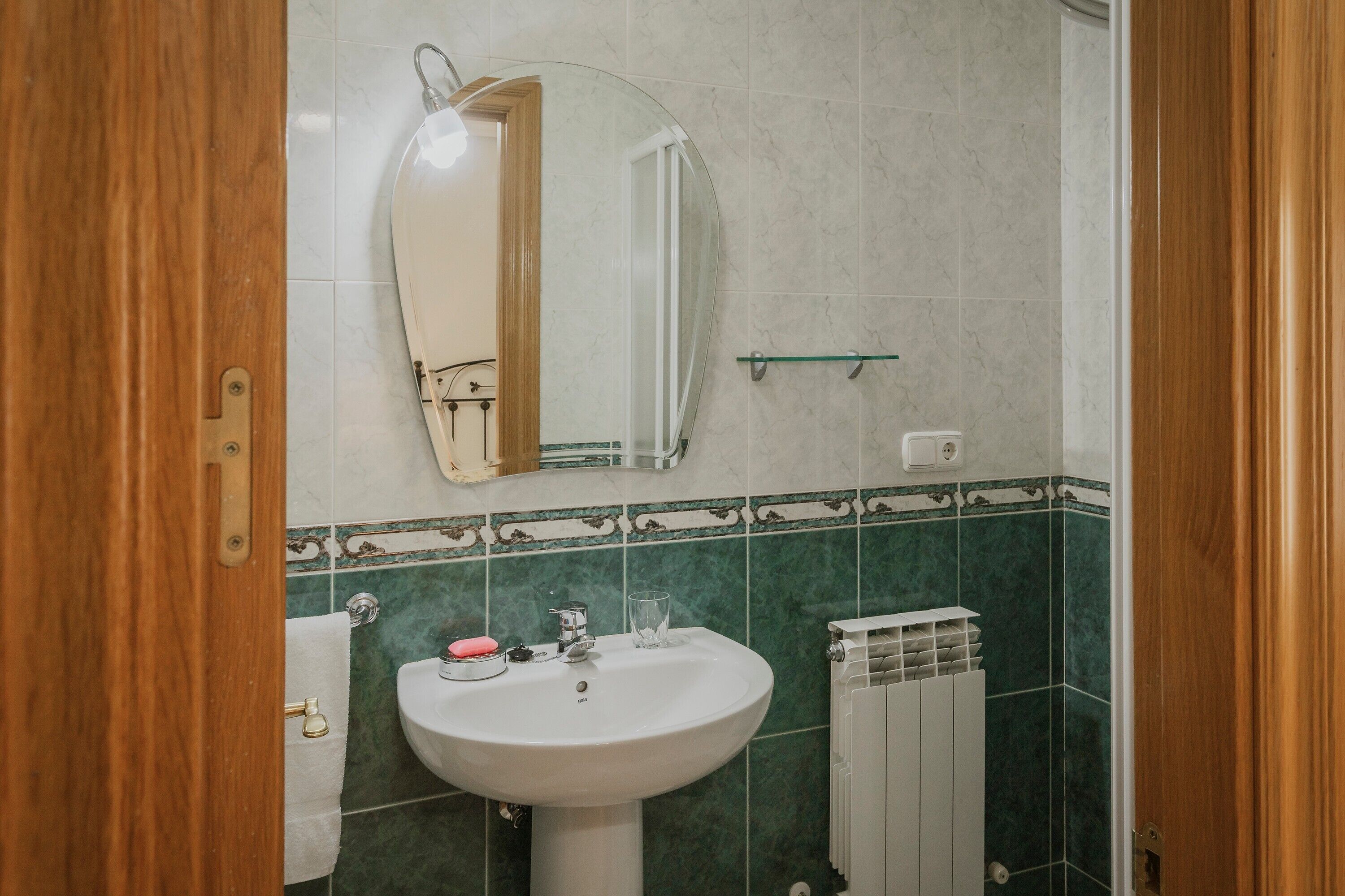 Ein Badezimmer mit weißem Waschbecken, einem Spiegel und grün gefliesten Wänden.