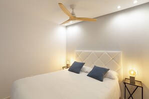 Quarto com cama, ventoinha no teto, luminárias de cabeceira e mesa de apoio.