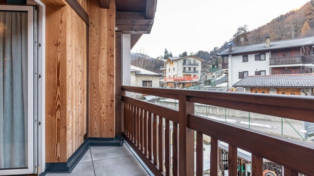 A wooden balcony with a view of a town and mountains. - Apartment 'Appartamento Condominio Genziana' with Mountain View, Balcony and Wi-Fi (Dimaro Folgarida)