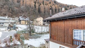 A residential area with houses, a snowy ground, and a forested hill in the background. - Apartment 'Appartamento Condominio Genziana' with Mountain View, Balcony and Wi-Fi (Dimaro Folgarida)