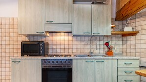 A kitchen with wooden cabinets, a microwave, a stove, and a sink. - Apartment 'Appartamento Condominio Genziana' with Mountain View, Balcony and Wi-Fi (Dimaro Folgarida)