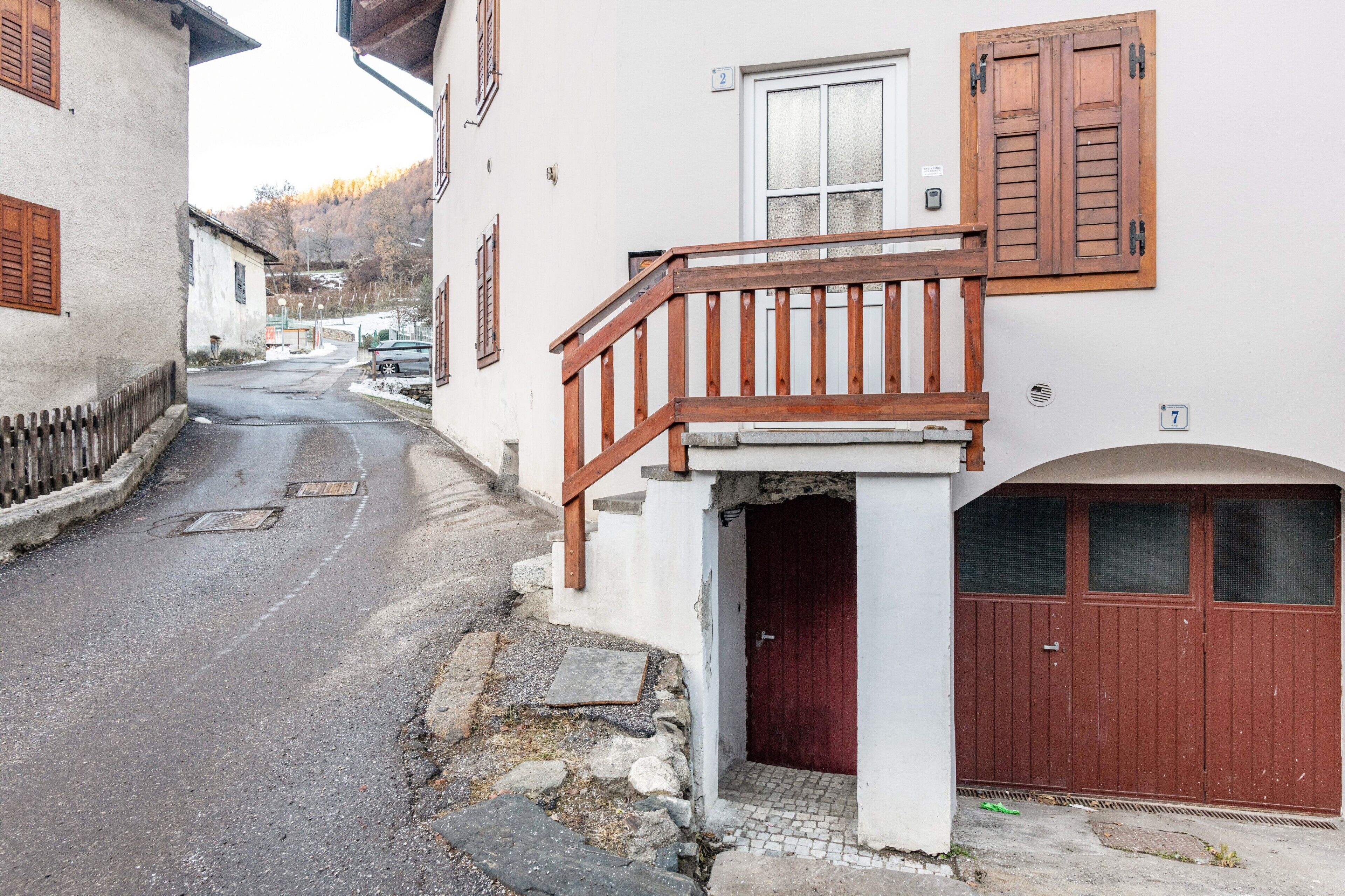 Une rue étroite bordée d’un immeuble blanc, doté d’un balcon en bois et d’une porte rouge.