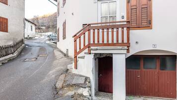 Une rue étroite bordée d’un immeuble blanc, doté d’un balcon en bois et d’une porte rouge.