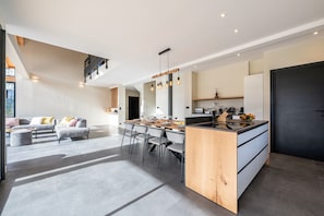 Et moderne køkken med en central ø, spiseplads med stole, og en trappe til et højere plan.