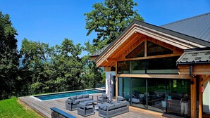 Una casa moderna con piscina, mobiliario exterior y grandes ventanales.
