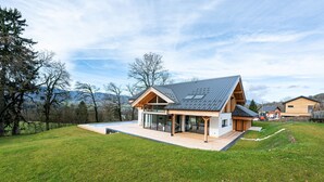 Una casa moderna con una amplia terraza, techo inclinado y vistas del paisaje circundante.