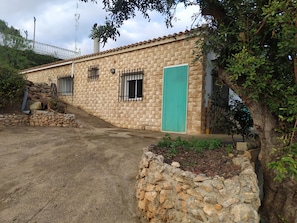 Un edificio de piedra con rejas en las ventanas, una puerta verde y un camino de entrada pavimentado.