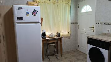 Cocina compacta con refrigerador, lavadora, una mesita con una silla y una ventana con cortina.