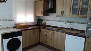 Eine kompakte Küche mit Holzausstattung, einem integrierten Geschirrspüler und einem Fenster mit Jalousien.