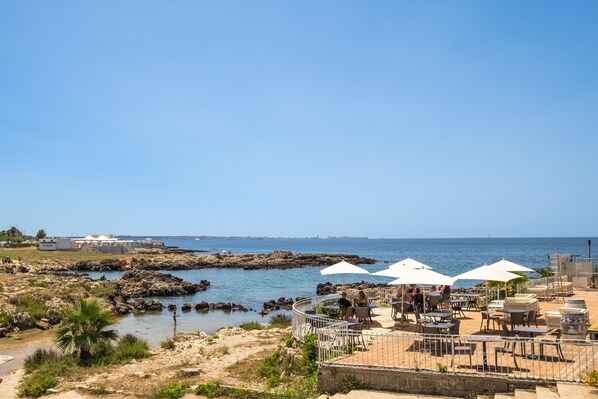 Un restaurante costero con terraza, un litoral rocoso y vistas al mar.