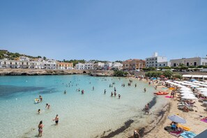Un pueblo costero con una playa, agua cristalina y edificios al fondo.