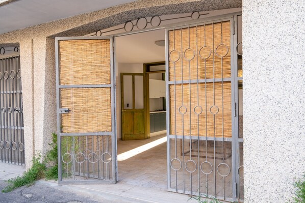 A gated entrance with a woven mat and metal bars, leading to a building with a visible interior door.