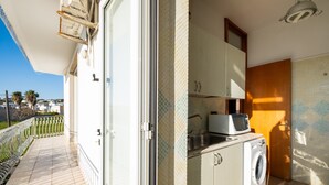 A balcony with a view of palm trees, a washing machine, and a microwave in a compact kitchen area.