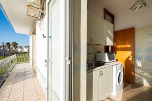 A balcony with a view of palm trees, a washing machine, and a microwave in a compact kitchen area.