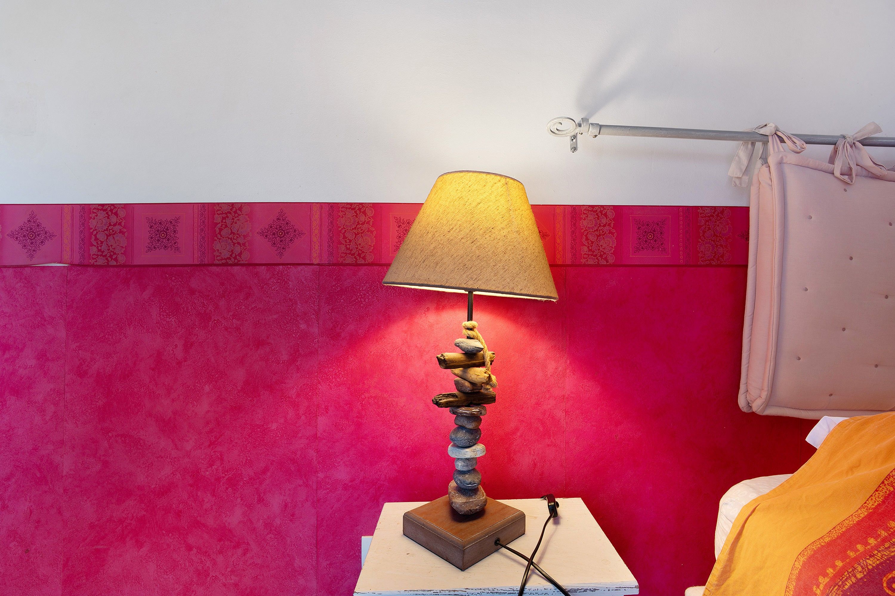 A lamp with a unique design on a wooden base, a red wall with a decorative border, and a white curtain.
