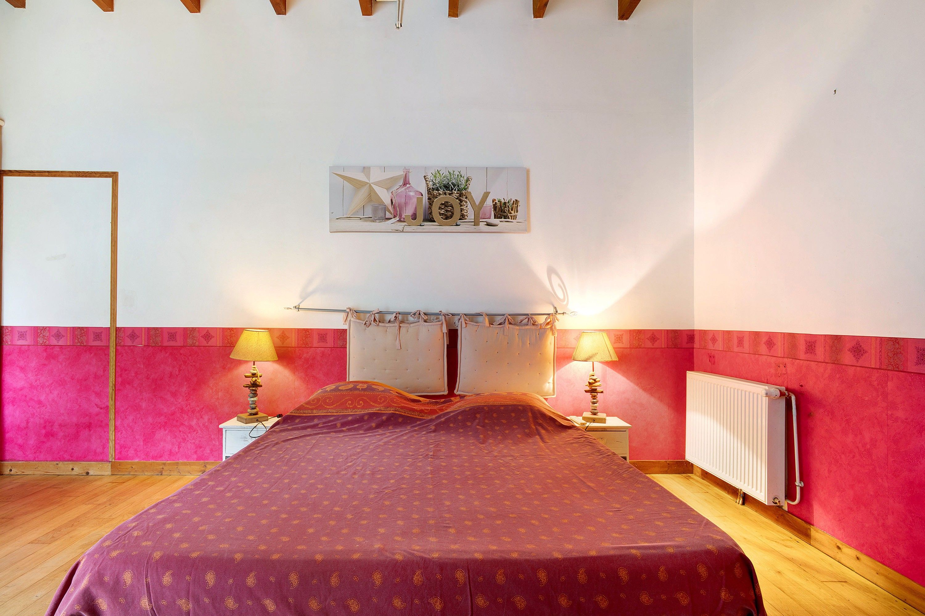 A bedroom with a bed, two bedside lamps, a radiator, and a wall-mounted artwork.