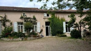 Un bâtiment à deux étages avec une allée gravillonnée, une porte d’entrée et un petit jardin agrémenté de plantes et de fleurs.