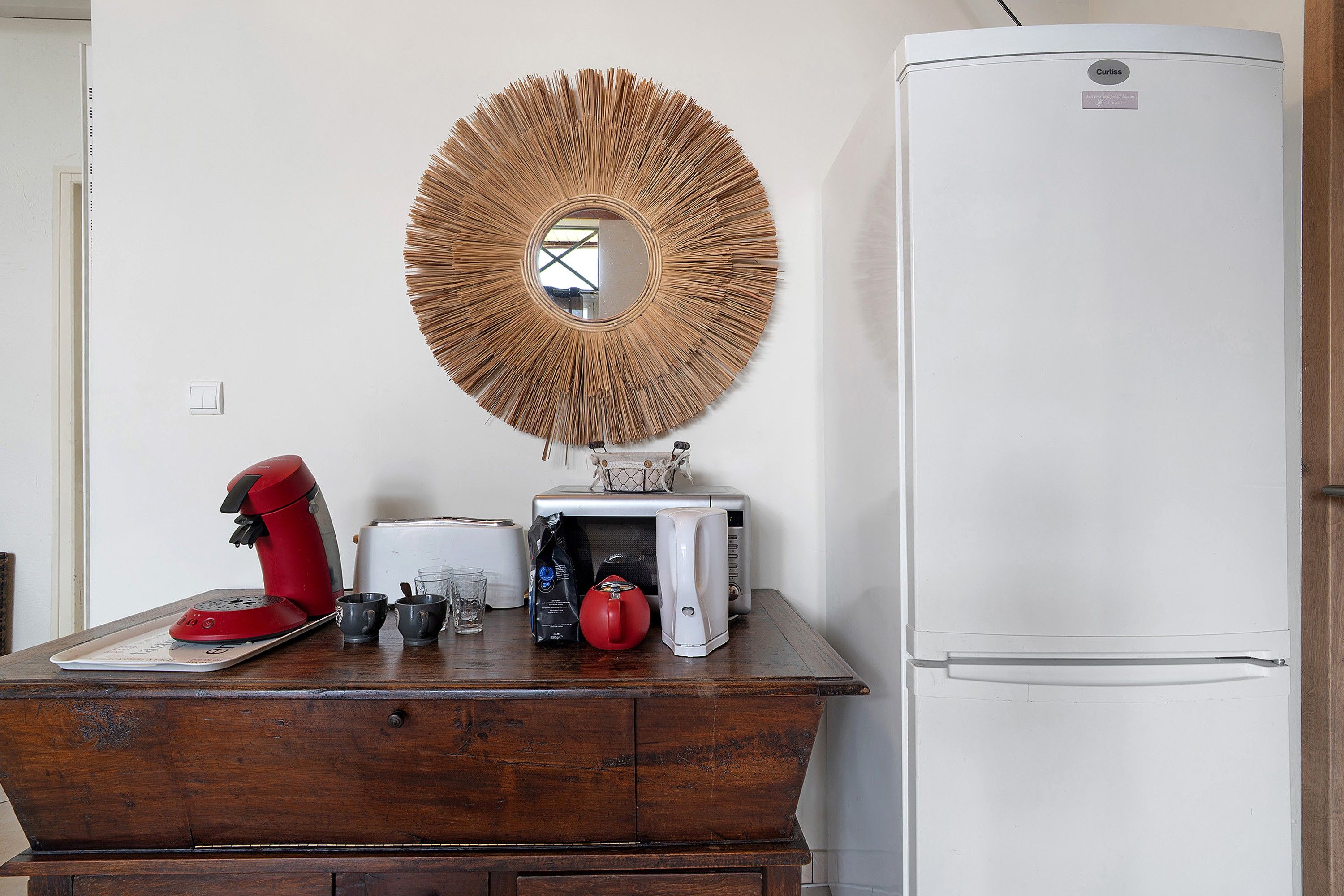 A kitchen with a white refrigerator, a wooden cabinet, a red coffee maker, a toaster, and a bag of coffee.