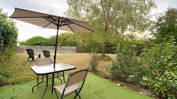 Une terrasse extérieure avec une table et des chaises, un grand parasol et une clôture en bois en arrière-plan.