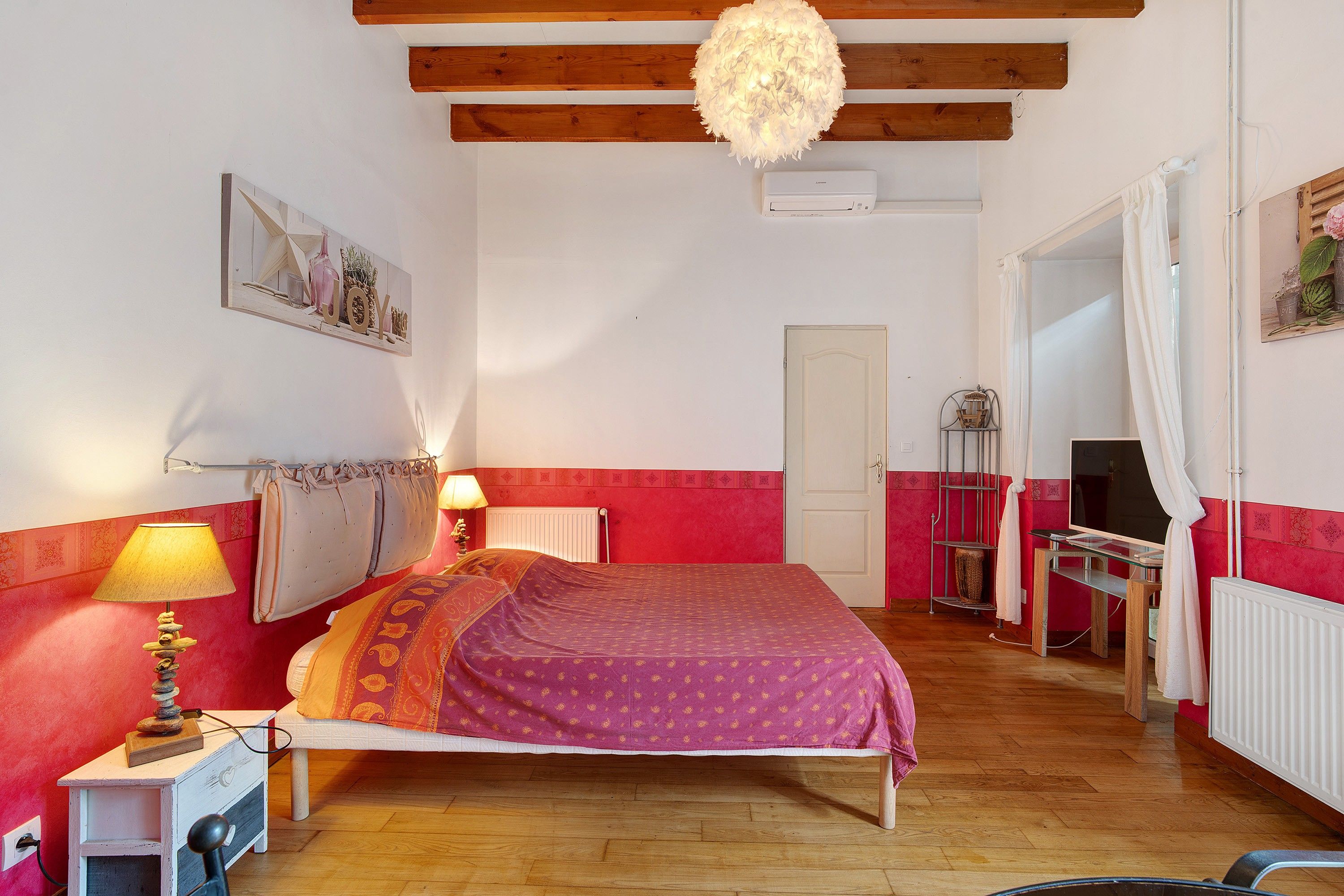 A bedroom with a bed, bedside lamps, a radiator, a television, and a door.