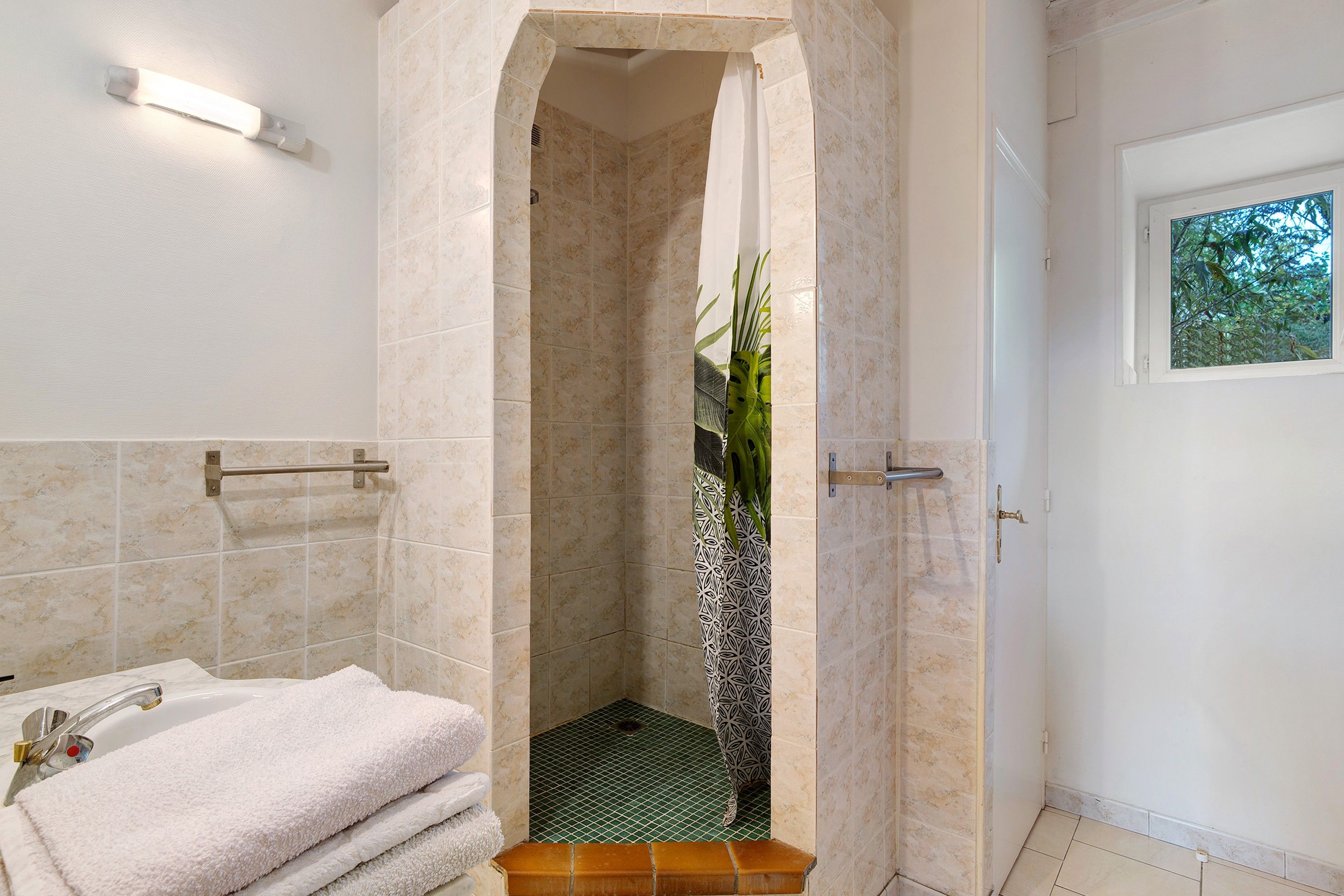 Un baño con bañera, ducha con cortina estampada y puerta con ventana.