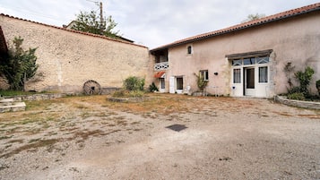 A rustic building with a stone wall, a gravel courtyard, and a traditional door.