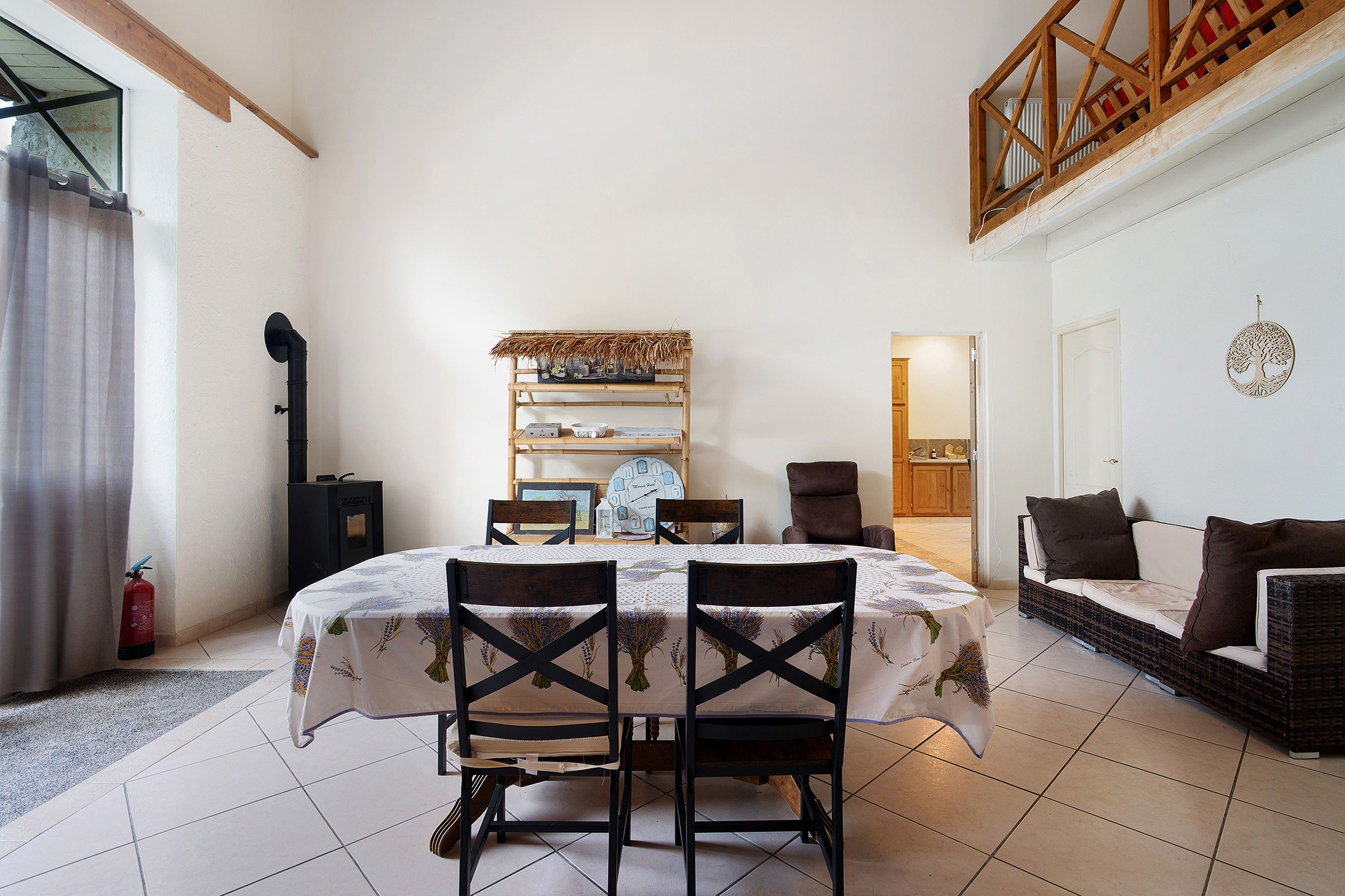 Een eetruimte met een tafel voor vier personen, omringd door stoelen, een wandplank met decoratieve objecten en uitzicht op een keuken.