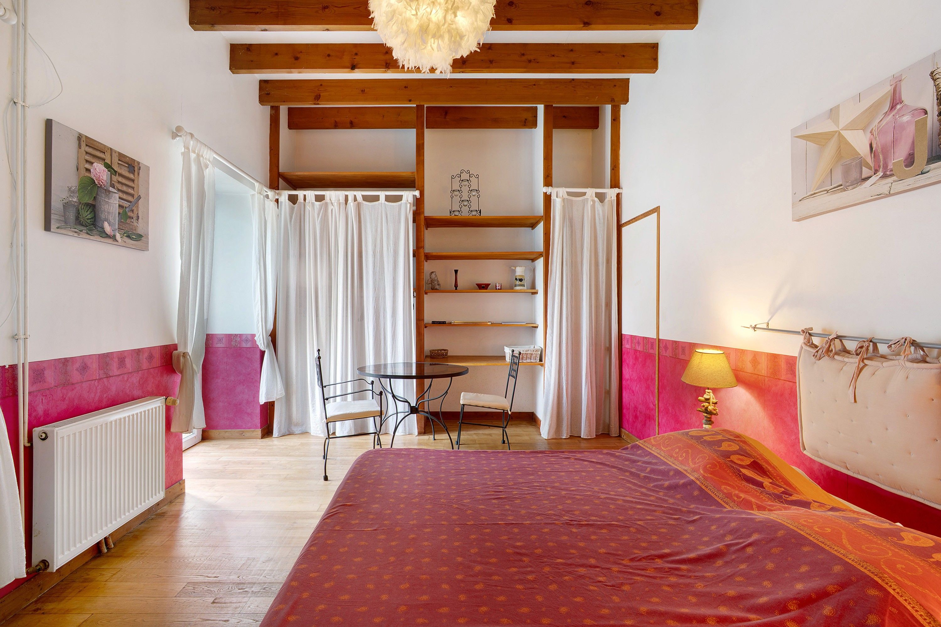 Une chambre à coucher comprenant un lit, une table, des chaises, un radiateur et une étagère ornée d’objets décoratifs.
