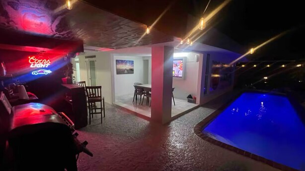A poolside area with a neon sign, a pool, and a seating area with a table and chairs.