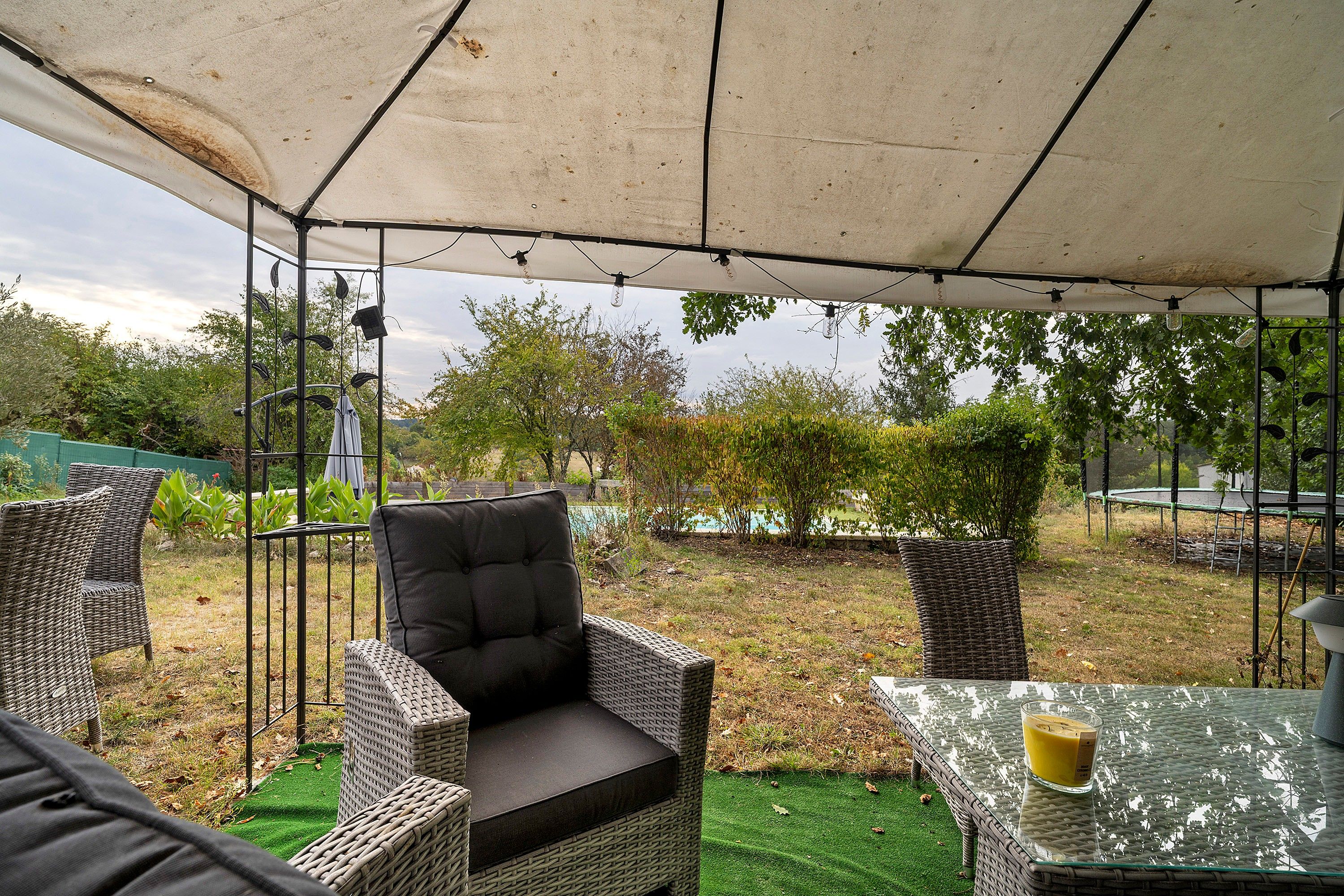 Een terras buiten met rieten meubilair, een glazen tafel en een overkapping.