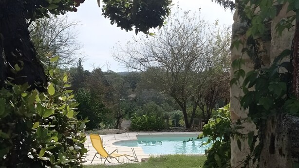 A backyard with a swimming pool, a yellow chair, and a stone wall.