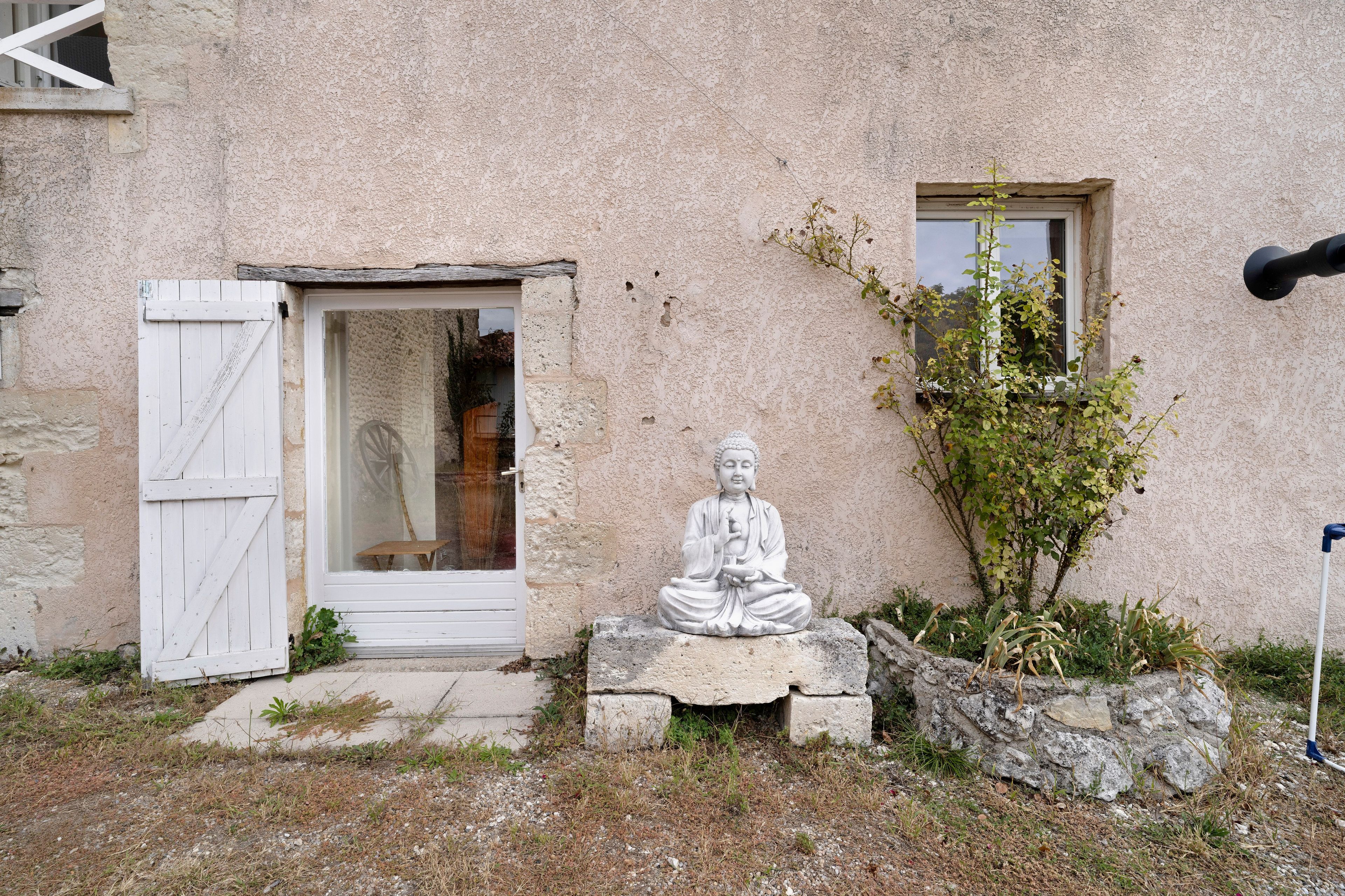 Une statue représentant une figure assise, située dans un jardin, avec un bâtiment en arrière-plan.