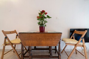 A wooden dining table with a red vase of flowers, two wooden chairs with cushions, and a tiled floor. - Terre Happy – Country House with Shared Pool in Ribérac (Ribérac)