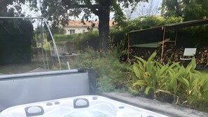 A hot tub with a control panel, surrounded by a garden with plants and a wooden structure.