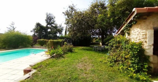 Un pati amb piscina, mur de pedra i zona enjardinada.