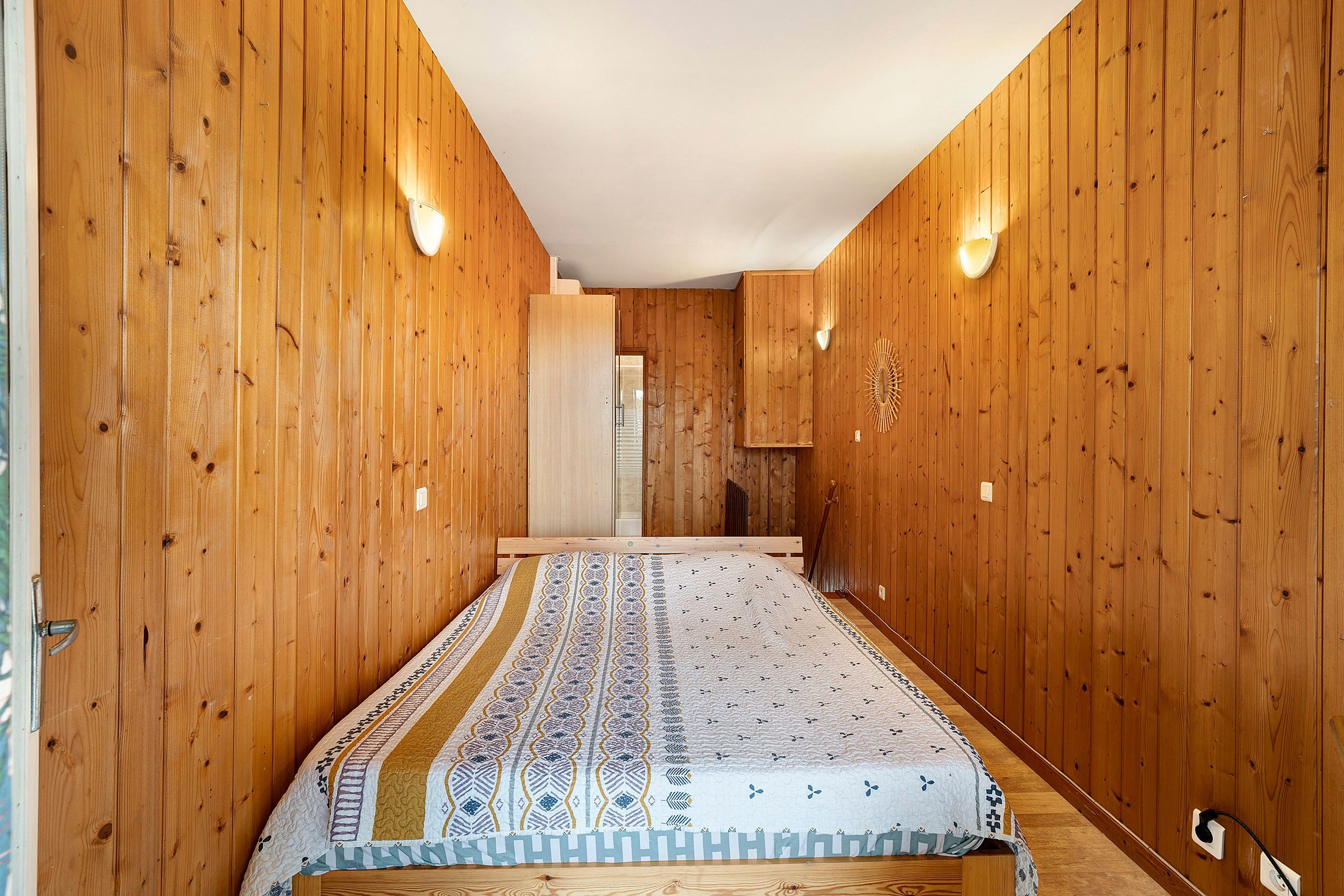 A narrow hallway with wooden walls and a patterned bedspread.