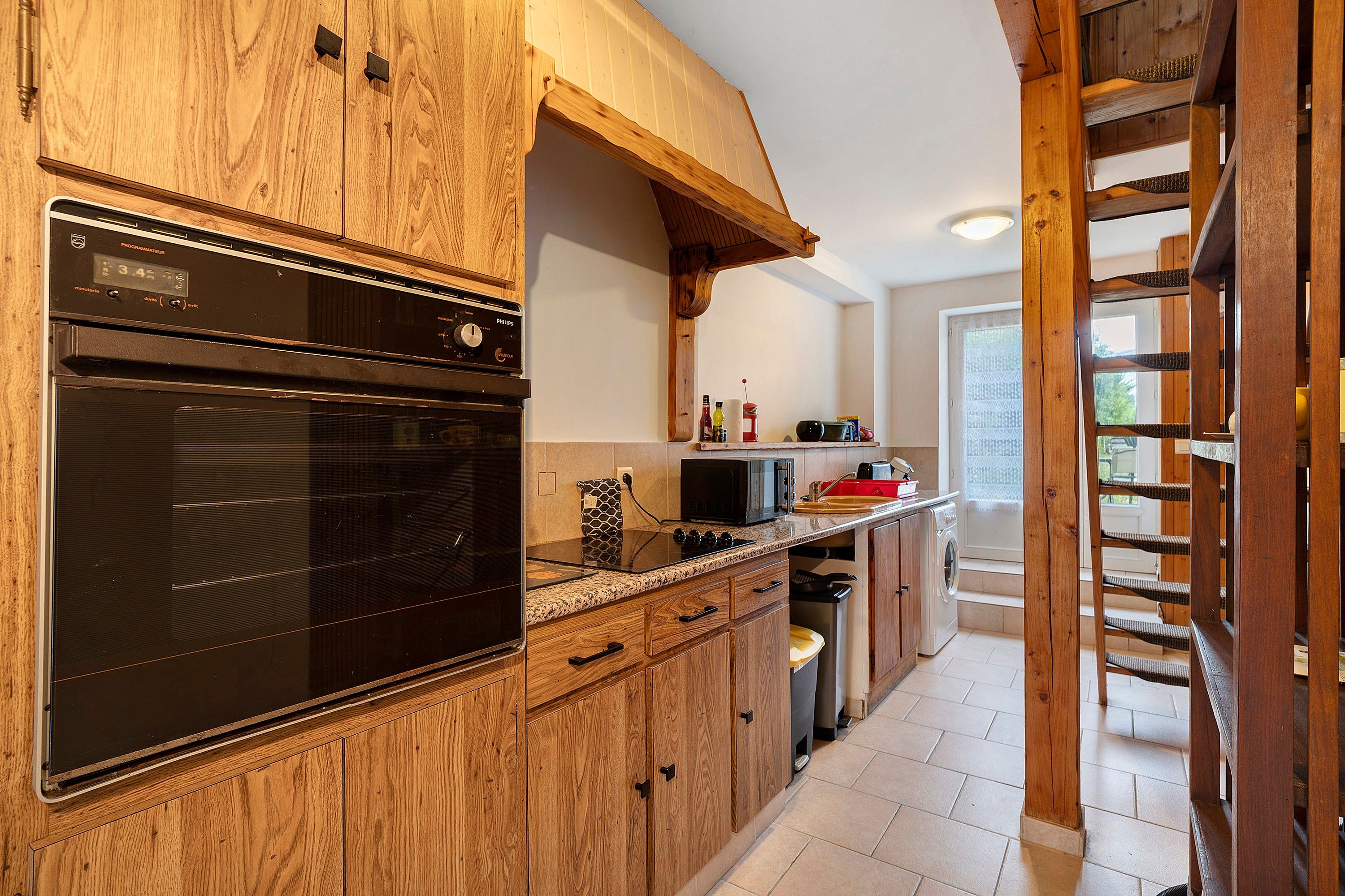 Eine Küche mit Holzausstattung, einem eingebauten Backofen, einer Mikrowelle und einem Edelstahl-Spülbecken.