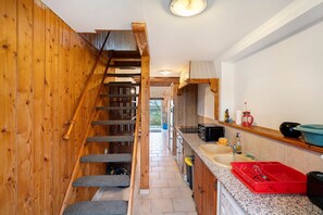Une cuisine étroite aux murs en bois, avec un escalier intégré et un évier surmonté d’un égouttoir rouge.